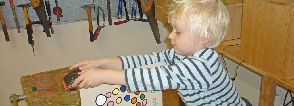 Bild 5 zeigt einen Jungen, der eifrig in der Werkstadt an Holz arbeitet.